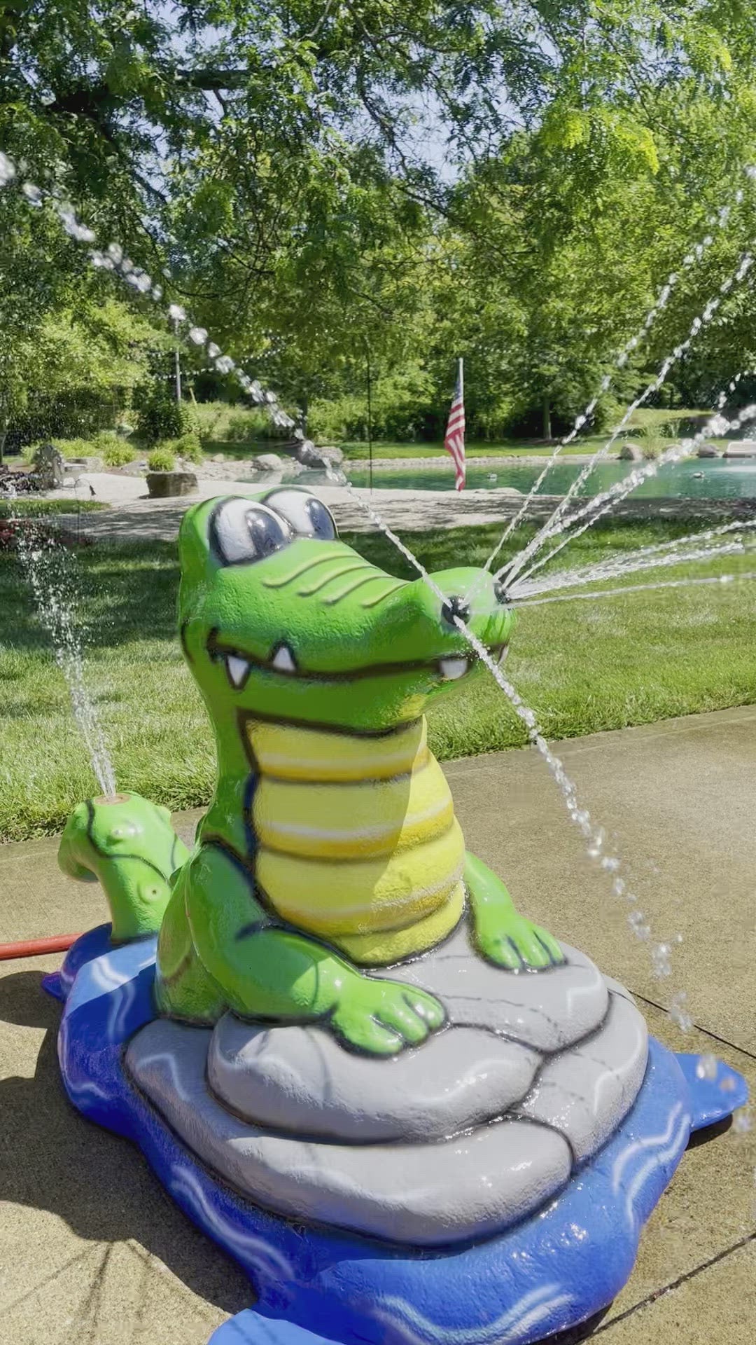 Alligator splash pad water play feature with bright green body and yellow belly, spraying water streams for kids’ outdoor fun.