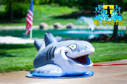 Shark-themed spray feature from My Splash Pad for backyard water play with patriotic flag and fountain in background
