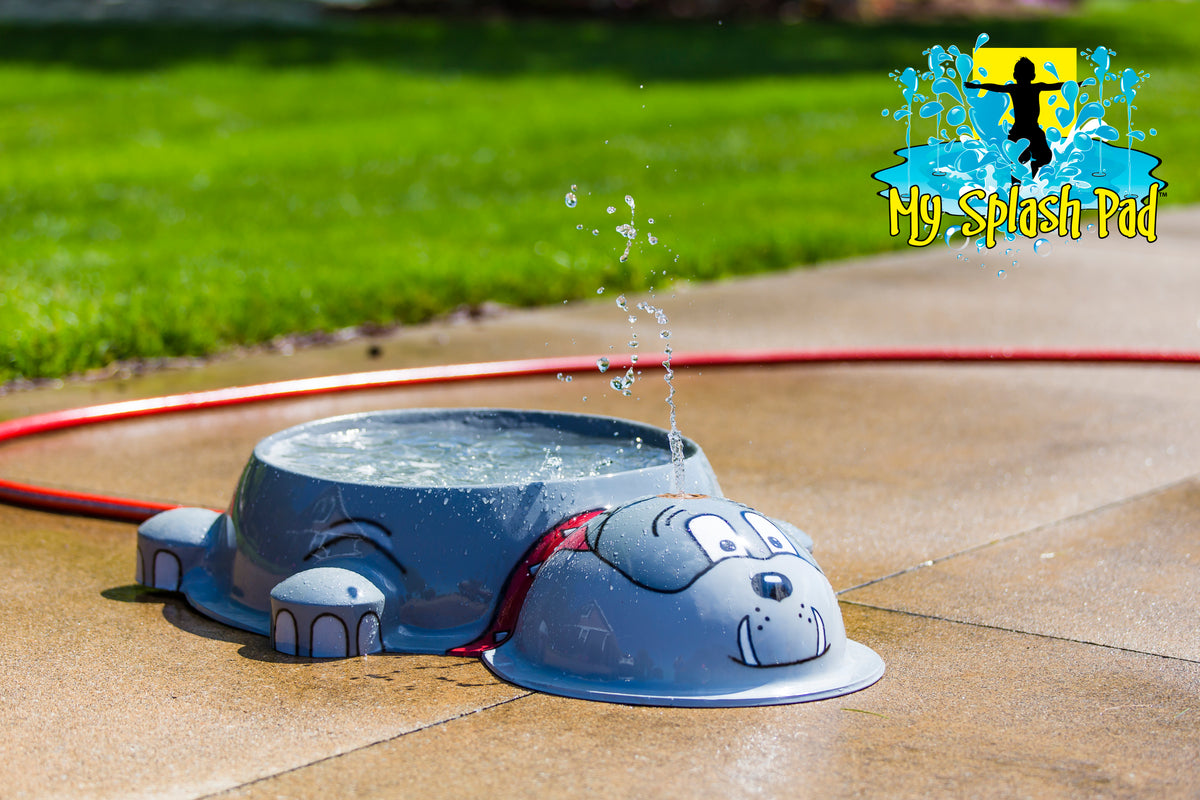 Dog Park Bulldog Water Bowl Water Play Feature by My Portable Splash Pad – gray bulldog-shaped water bowl spraying water on outdoor concrete with red hose and grass in background.