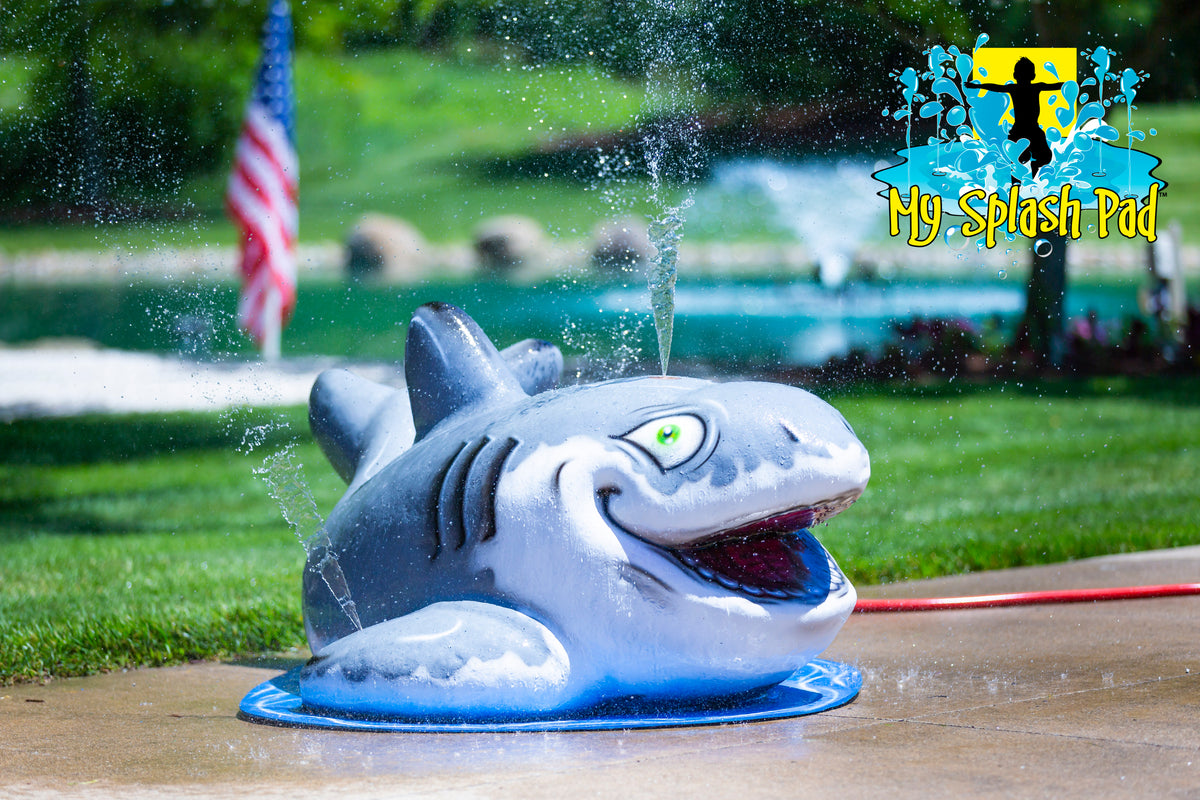 Shark-shaped mobile water play feature with a wide open mouth, green eyes, and detailed fins, designed for children’s splash pad play.